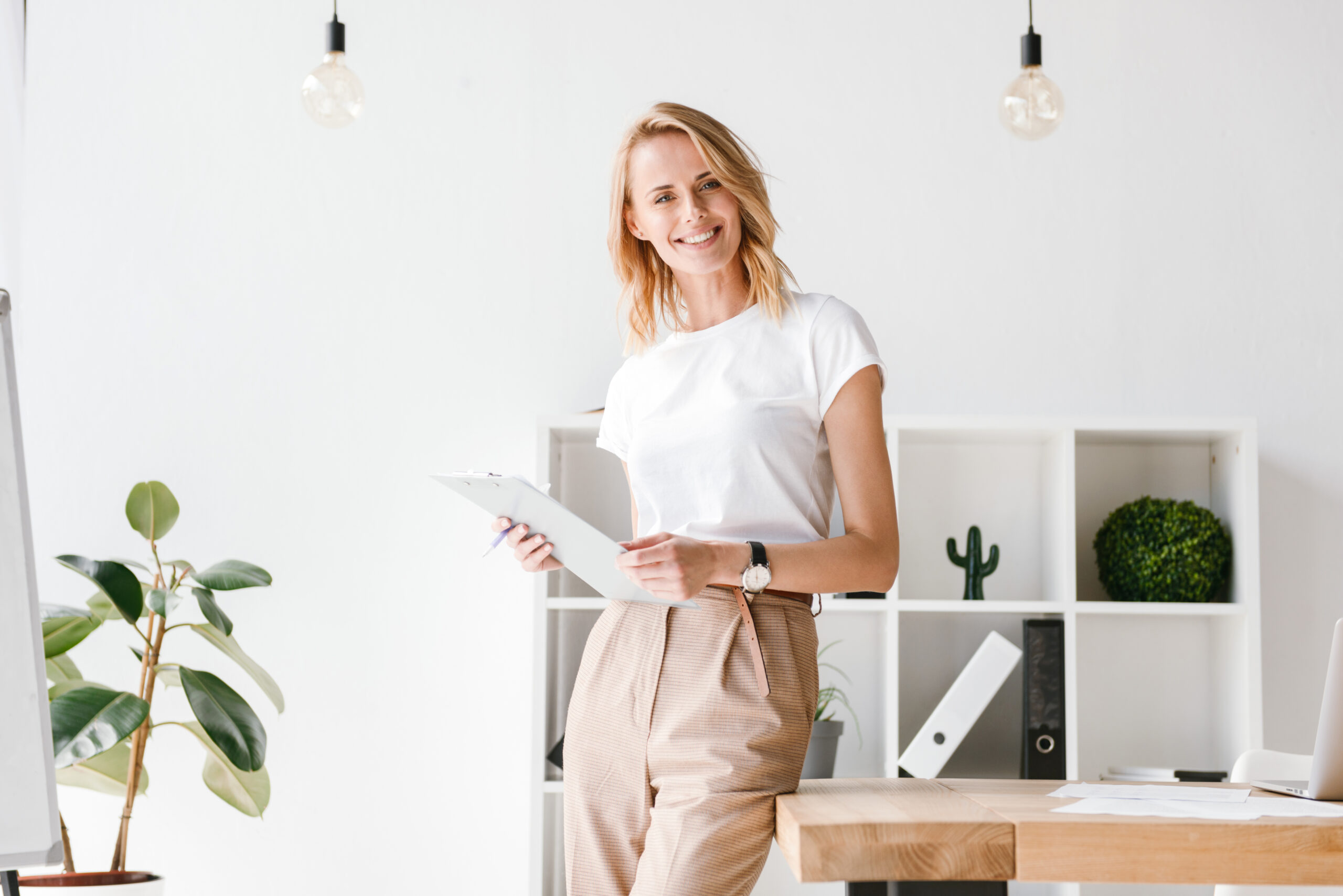Smiling businesswoman holding folder while leaning on a office desk